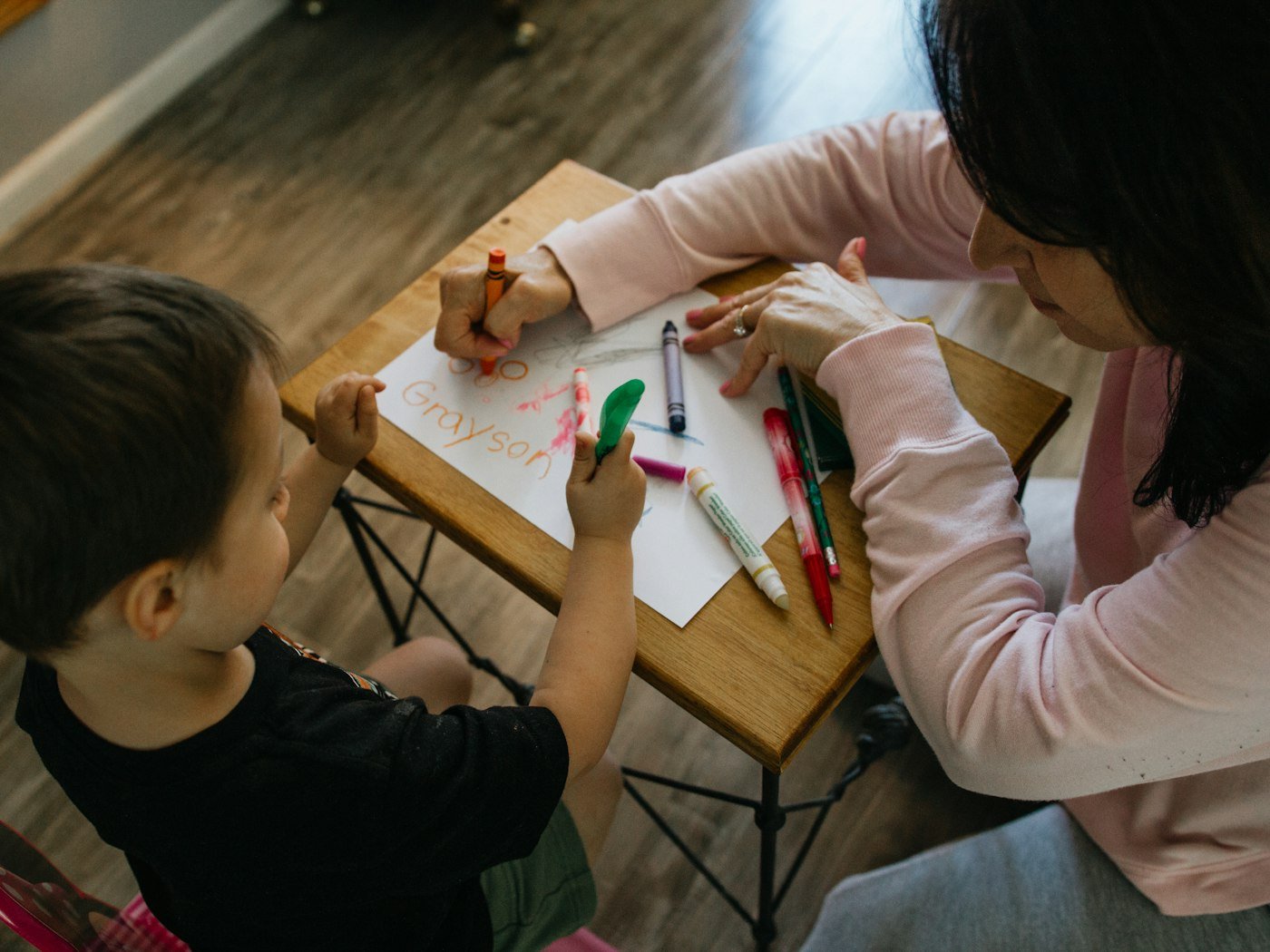 A therapist and a young child drawing together with crayons at a low table