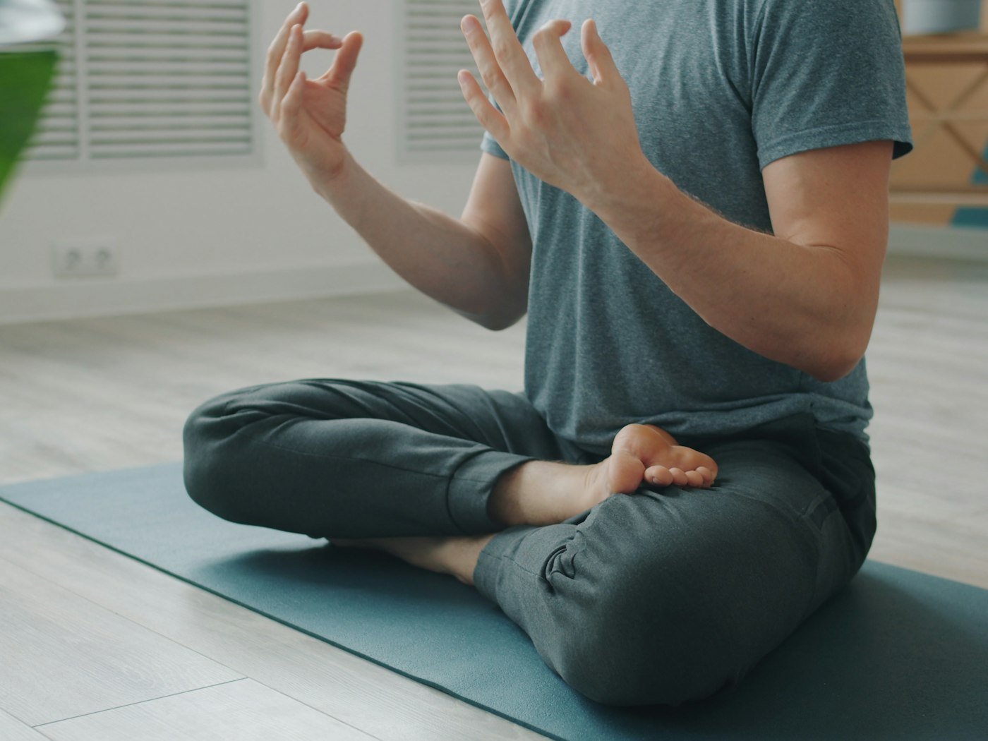 A person seated cross-legged in meditation on a mat in a calm, bright room