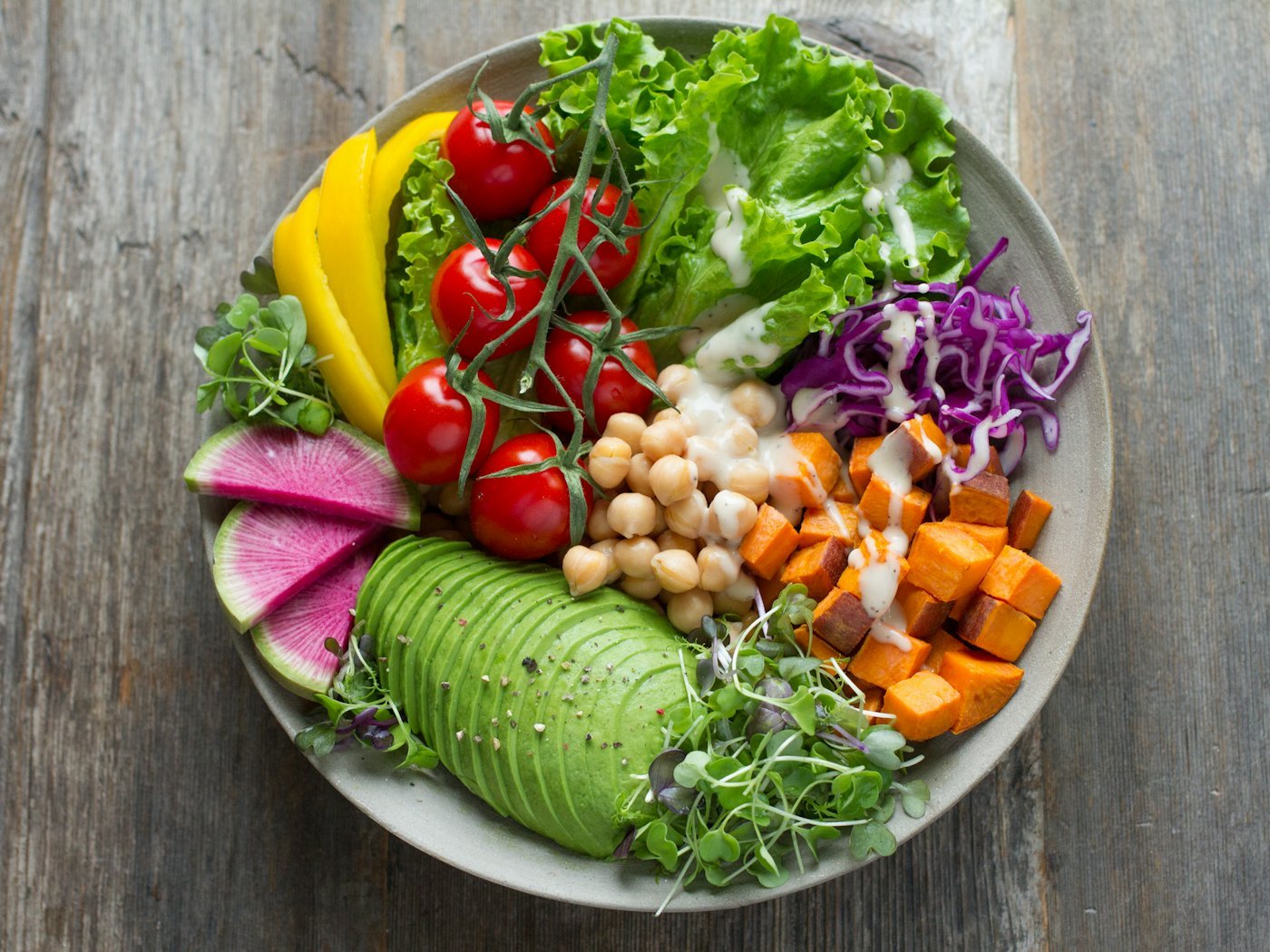A colourful bowl of fresh vegetables, chickpeas and avocado on a wooden table
