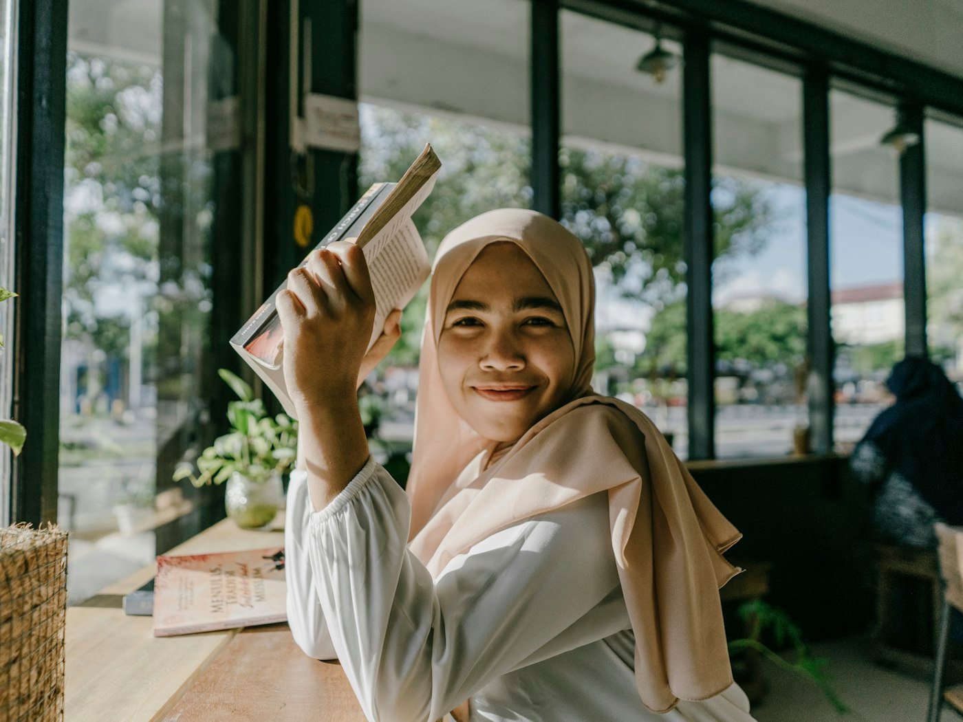 A smiling student holding a book beside a bright window